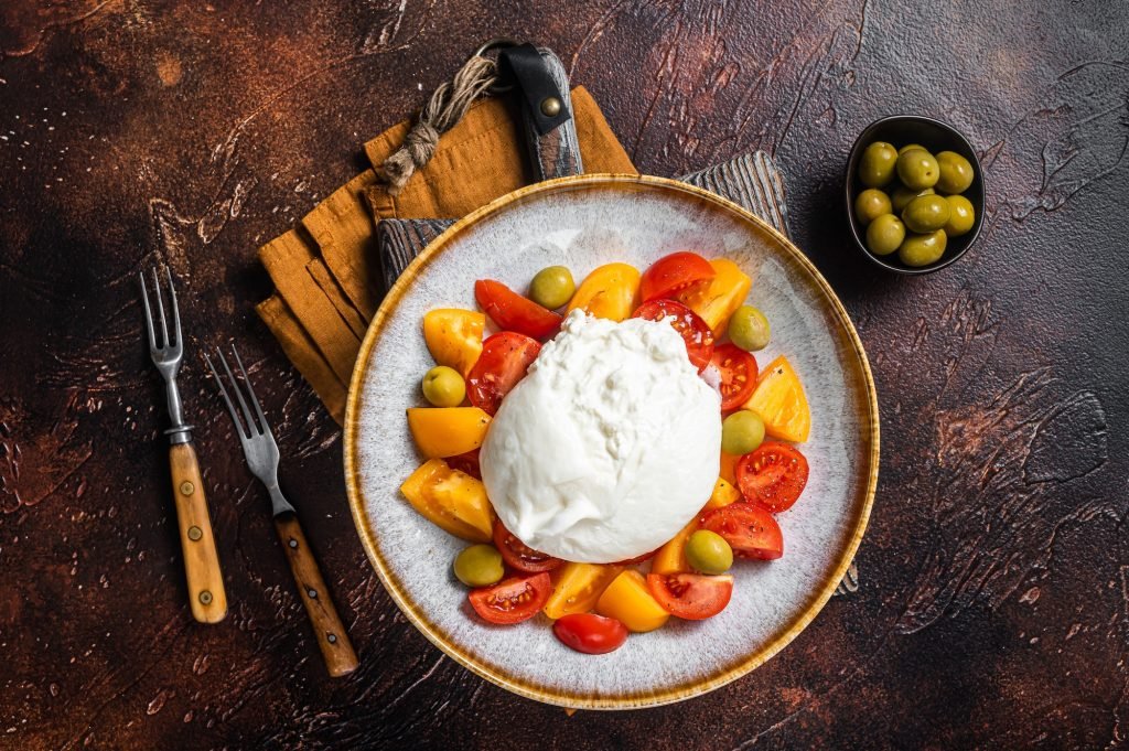 Burrata cheese and tomatoes salad served on rustic plate. Dark background. Top view