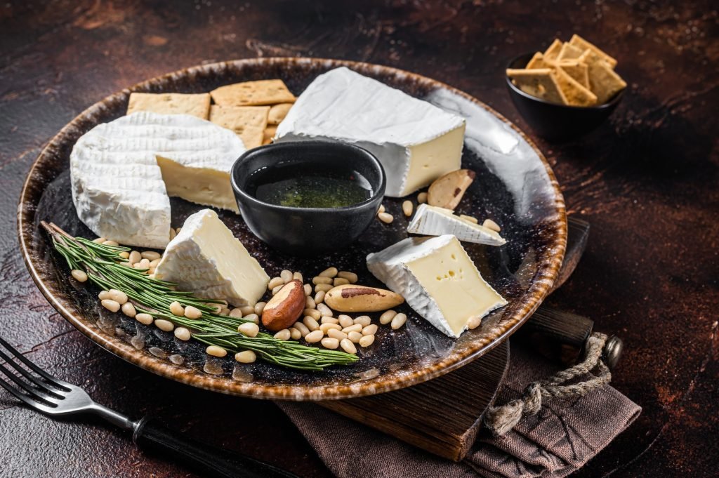 Cheese plate with brie and camembert on rustic plate with nuts and honey. Dark background. Top view