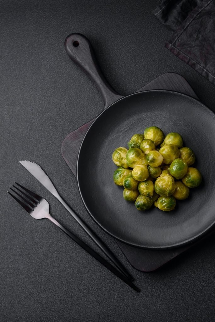 Delicious boiled Brussels sprouts on a ceramic plate on a dark concrete background