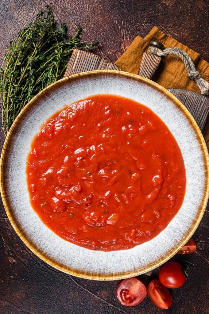 Homemade tomato Passata in rustic plate with herbs. Dark background. Top view