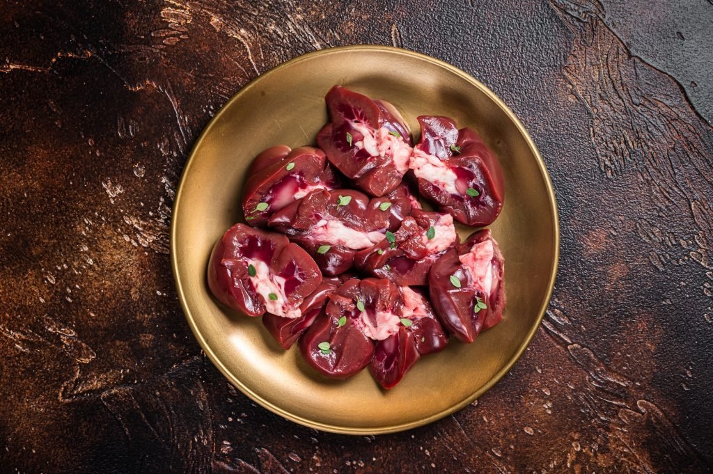 Raw Beef kidney, fresh sliced offal meat on plate. Dark background. Top view