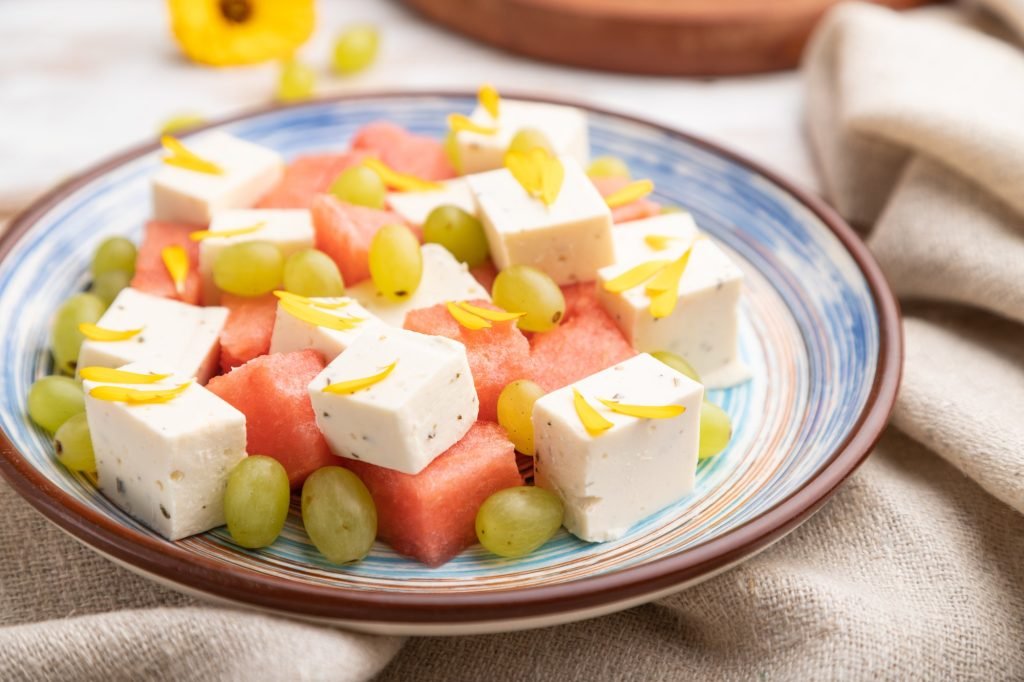 Vegetarian salad with watermelon, feta cheese, and grapes on blue ceramic plate on white